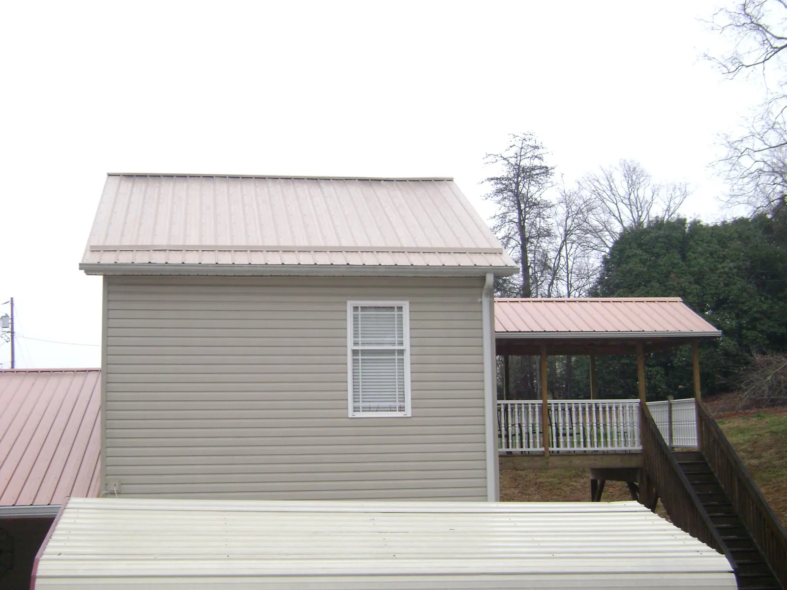 Tan metal roofs on a two story addition and attached porch, from a Roof Replacement job in Cameron